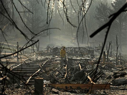 In this Nov. 16, 2018, file photo, a firefighter searches for human remains in a trailer park destroyed in the Camp Fire, in Paradise, Calif. The massive wildfire that killed dozens of people and destroyed thousands of homes has been fully contained after burning for more than two weeks, authorities said Sunday, Nov. 25. (AP Photo/John Locher, File)